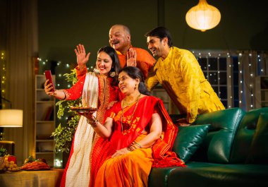 Diwali kutlaması sırasında selfie çeken, kıdemli ebeveynleri ve yetişkin çocukları olan Hintli aile akşam şenliklerinde birlikte oturan, ışıklarla süslenmiş, rahat koltukta mutlu bir şekilde gülümseyen.