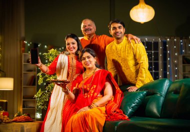 Kameraya boş akıllı telefon ekranı gösteren Hintli aile, genç oğlu ve kızı olan aile Diwali festivali sırasında rahat koltukta oturuyor, gülümsüyor ürün veya servisi tanıtıyor.