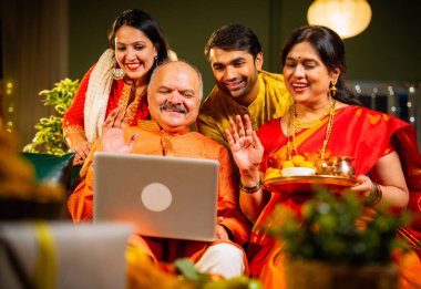 Video konferansında Diwali 'nin mutlu olmasını dileyen dört kişilik Hintli aile, aile büyükleri, yetişkin oğulları ve kızları akşamları kapalı koltukta oturmuş akrabalarını selamlamak için akıllı telefon kullanıyorlar.