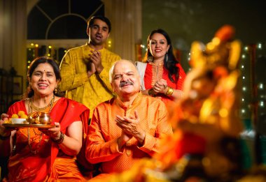 Ganesh Chaturthi sırasındaki Ganesha putuna odaklanın. Hintli aile, büyük anne-baba, oğul, gelin laddu tabağı ve puja thali ile süslenmiş festival evinde dua edin.