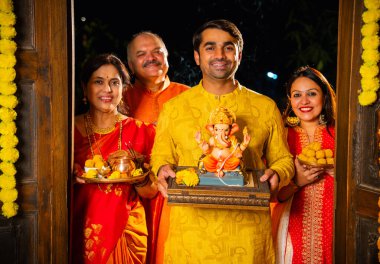 Ganesh Chaturthi sırasındaki Ganesha 'nın kil heykelini Hintli bir aile, yaşlı bir aile ve genç bir çift karşılıyor Ganpati' yi laddu ve puja thali ile dekore edilmiş evin girişinde ibadet için eve getiriyorlar.