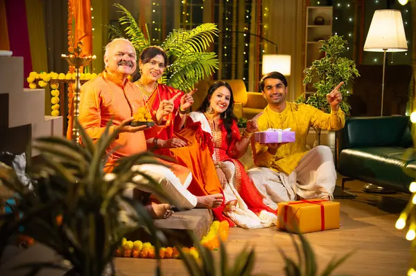 Ladus 'u kucaklayan ve birlikte gülümseyen Hintli aile, genç bir kızla birlikte, sari giymiş yaşlı bir anne, geleneksel giysili baba ve koca Diwali' yi kapalı mekanda kutluyor, çiçek rangoli ve kahkahalarla.