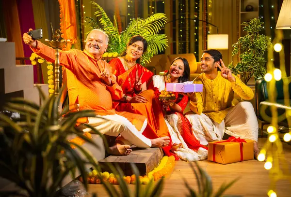 Latdu 'yla Diwali selfie, genç kızla Hintli aile, sari giyen yaşlı anne, geleneksel giyimli baba ve koca Hindu festivalini dekore edilmiş evde diya rangoli ile kutluyorlar.
