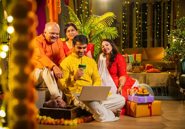 İnternetten bilgisayar ve kredi kartı kullanarak alışveriş yapan, karısı olan Hintli genç adam, geleneksel kıdemli ebeveynler evde Diwali gecesini kutluyorlar, para, çiçek ve ev dekorasyonlarıyla birlikte oturuyorlar.