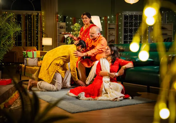 Oğul, anne ve babasından Diwali duası almak için şenlikli bir evde anne, baba ve genç kız oğulla sıcak bir jestle selamlaştıktan sonra televizyonda komik bir program izliyorlar.