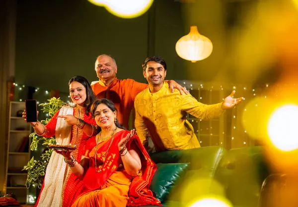 Kameraya boş akıllı telefon ekranı gösteren Hintli aile, genç oğlu ve kızı olan aile Diwali festivali sırasında rahat koltukta oturuyor, gülümsüyor ürün veya servisi tanıtıyor.