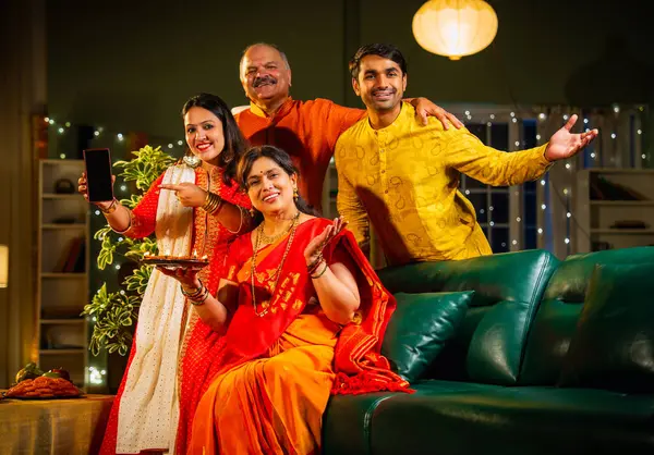 Kameraya boş akıllı telefon ekranı gösteren Hintli aile, genç oğlu ve kızı olan aile Diwali festivali sırasında rahat koltukta oturuyor, gülümsüyor ürün veya servisi tanıtıyor.