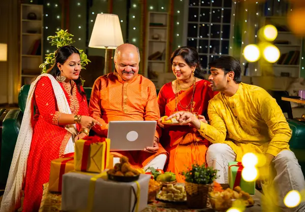 Video konferansında Diwali 'nin mutlu olmasını dileyen dört kişilik Hintli aile, aile büyükleri, yetişkin oğulları ve kızları akşamları kapalı koltukta oturmuş akrabalarını selamlamak için akıllı telefon kullanıyorlar.
