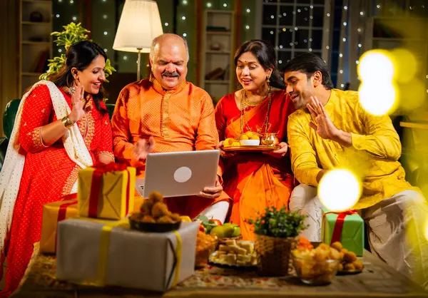Video konferansında Diwali 'nin mutlu olmasını dileyen dört kişilik Hintli aile, aile büyükleri, yetişkin oğulları ve kızları akşamları kapalı koltukta oturmuş akrabalarını selamlamak için akıllı telefon kullanıyorlar.
