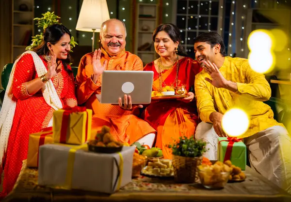 Video konferansında Diwali 'nin mutlu olmasını dileyen dört kişilik Hintli aile, aile büyükleri, yetişkin oğulları ve kızları akşamları kapalı koltukta oturmuş akrabalarını selamlamak için akıllı telefon kullanıyorlar.