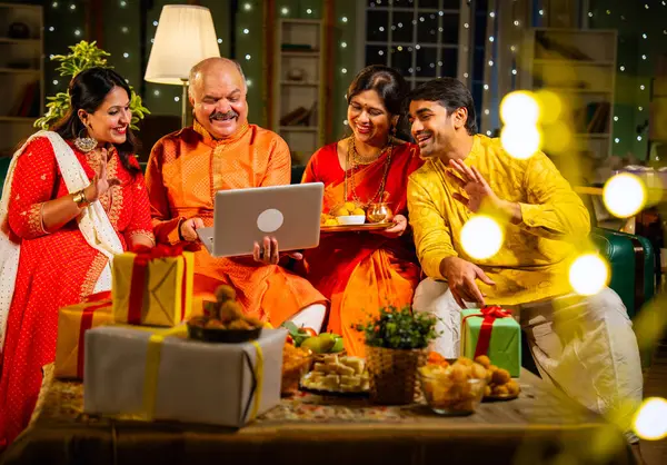 Video konferansında Diwali 'nin mutlu olmasını dileyen dört kişilik Hintli aile, aile büyükleri, yetişkin oğulları ve kızları akşamları kapalı koltukta oturmuş akrabalarını selamlamak için akıllı telefon kullanıyorlar.