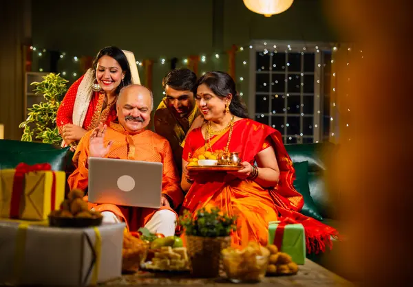 Video konferansında Diwali 'nin mutlu olmasını dileyen dört kişilik Hintli aile, aile büyükleri, yetişkin oğulları ve kızları akşamları kapalı koltukta oturmuş akrabalarını selamlamak için akıllı telefon kullanıyorlar.