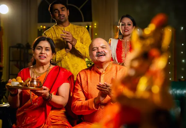 Ganesh Chaturthi sırasındaki Ganesha putuna odaklanın. Hintli aile, büyük anne-baba, oğul, gelin laddu tabağı ve puja thali ile süslenmiş festival evinde dua edin.