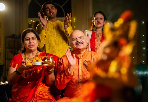 Ganesh Chaturthi sırasındaki Ganesha putuna odaklanın. Hintli aile, büyük anne-baba, oğul, gelin laddu tabağı ve puja thali ile süslenmiş festival evinde dua edin.