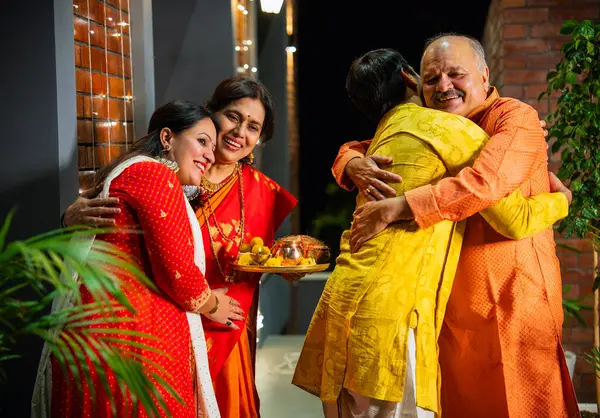 Diwali akşamında damat ve gelini karşılayan Hintli üst düzey aileler, ziyaretçi çifti sımsıkı kucaklıyor, gülümsüyor ve güzel dekore edilmiş ev girişlerine kahkahalarla gülüyor.