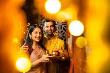 Geleneksel etnik kıyafetli Hintli genç çift puja thali ile birlikte Hint Diwali festivali ya da yeni eve neşeyle girerken karşılama töreni için namaskar yapıyorlar.