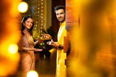 Geleneksel etnik kıyafetli Hintli genç çift puja thali ile birlikte Hint Diwali festivali ya da yeni eve neşeyle girerken karşılama töreni için namaskar yapıyorlar.