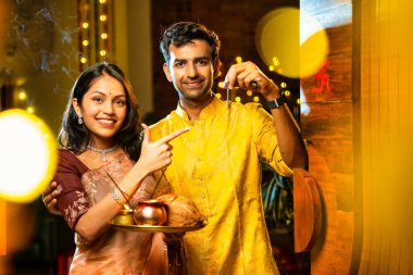 Gamalı haç çizerek ev anahtarlarını puja thali ile gösteriyorlar. Geleneksel Hintli genç çift fotoğraf makinelerini Hindu Diwali festivalindeki yeni evlerine girerken sevinçle selamlıyorlar.