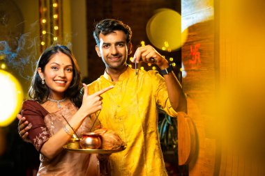 Gamalı haç çizerek ev anahtarlarını puja thali ile gösteriyorlar. Geleneksel Hintli genç çift fotoğraf makinelerini Hindu Diwali festivalindeki yeni evlerine girerken sevinçle selamlıyorlar.