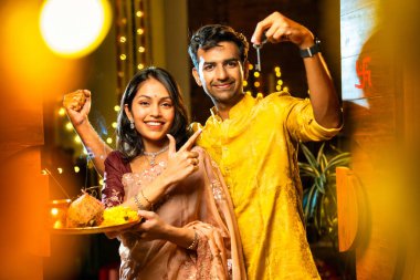 Gamalı haç çizerek ev anahtarlarını puja thali ile gösteriyorlar. Geleneksel Hintli genç çift fotoğraf makinelerini Hindu Diwali festivalindeki yeni evlerine girerken sevinçle selamlıyorlar.