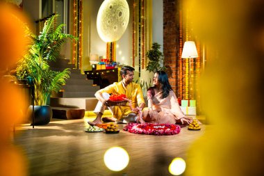 Geleneksel etnik kıyafetli Hintli çift, çiçekli çelenkler, ışıklar ve şenlikli neşeyle süslenmiş, neşeli havasıyla Diwali gecesinin tadını çıkarıyor.