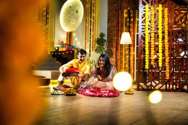 Geleneksel etnik kıyafetli Hintli çift, çiçekli çelenkler, ışıklar ve şenlikli neşeyle süslenmiş, neşeli havasıyla Diwali gecesinin tadını çıkarıyor.