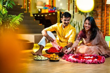 Geleneksel etnik kıyafetli Hintli çift, çiçekli çelenkler, ışıklar ve şenlikli neşeyle süslenmiş, neşeli havasıyla Diwali gecesinin tadını çıkarıyor.