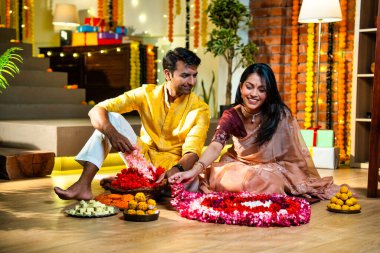Geleneksel etnik kıyafetli Hintli çift, çiçekli çelenkler, ışıklar ve şenlikli neşeyle süslenmiş, neşeli havasıyla Diwali gecesinin tadını çıkarıyor.