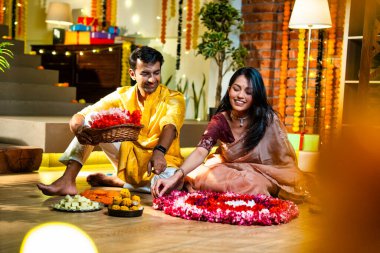 Geleneksel etnik kıyafetli Hintli çift, çiçekli çelenkler, ışıklar ve şenlikli neşeyle süslenmiş, neşeli havasıyla Diwali gecesinin tadını çıkarıyor.