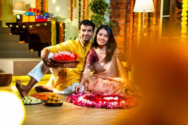 Geleneksel etnik kıyafetli Hintli çift, çiçekli çelenkler, ışıklar ve şenlikli neşeyle süslenmiş, neşeli havasıyla Diwali gecesinin tadını çıkarıyor.