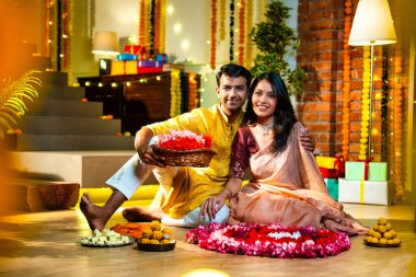 Geleneksel etnik kıyafetli Hintli çift, çiçekli çelenkler, ışıklar ve şenlikli neşeyle süslenmiş, neşeli havasıyla Diwali gecesinin tadını çıkarıyor.
