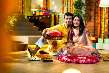 Geleneksel etnik kıyafetli Hintli çift, çiçekli çelenkler, ışıklar ve şenlikli neşeyle süslenmiş, neşeli havasıyla Diwali gecesinin tadını çıkarıyor.