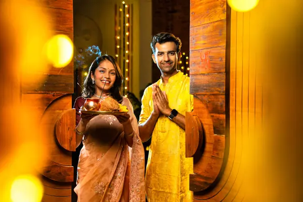 Geleneksel etnik kıyafetli Hintli genç çift puja thali ile birlikte Hint Diwali festivali ya da yeni eve neşeyle girerken karşılama töreni için namaskar yapıyorlar.