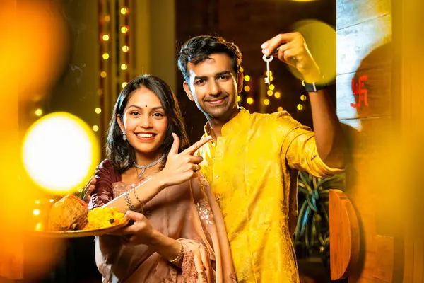 Gamalı haç çizerek ev anahtarlarını puja thali ile gösteriyorlar. Geleneksel Hintli genç çift fotoğraf makinelerini Hindu Diwali festivalindeki yeni evlerine girerken sevinçle selamlıyorlar.