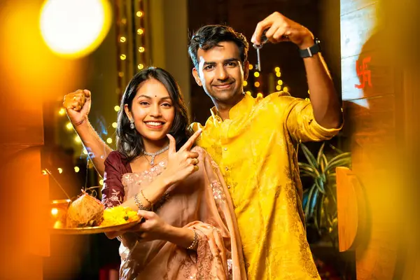 Gamalı haç çizerek ev anahtarlarını puja thali ile gösteriyorlar. Geleneksel Hintli genç çift fotoğraf makinelerini Hindu Diwali festivalindeki yeni evlerine girerken sevinçle selamlıyorlar.