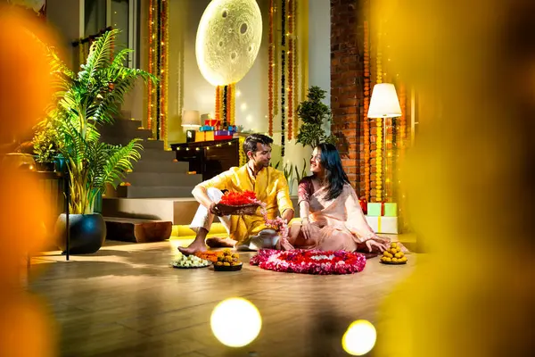 Geleneksel etnik kıyafetli Hintli çift, çiçekli çelenkler, ışıklar ve şenlikli neşeyle süslenmiş, neşeli havasıyla Diwali gecesinin tadını çıkarıyor.