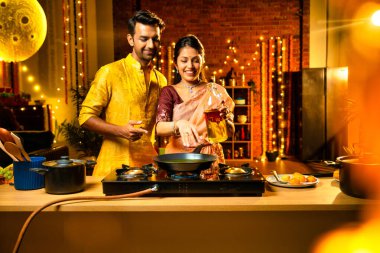 Diwali gecelerinde yemek pişirmek için tencereye yenilebilir yağ döken Hintli genç çift, aydınlatma ve çiçeklerle süslenmiş bir mutfakta birlikte yemek hazırlıyor ve neşeli bir havayla kutlama yapıyorlar.