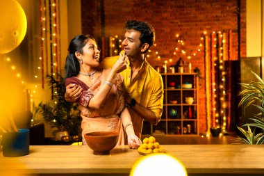 Hint çifti Diwali 'de süslü mutfakta laddu yapıyor. Işıklar ve çiçek çelenkleriyle dolu, neşe içinde geleneksel laddoo' yu hazırlıyor, sergiliyor ya da birlikte yiyor.