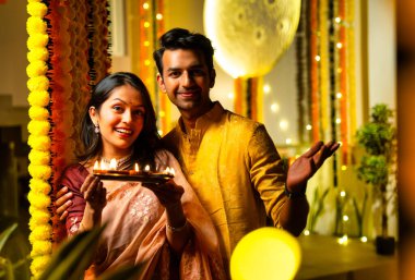 Geleneksel etnik kıyafetli Hintli çift, bayram gecesi Hindu festivali kutlamalarında renkli kadife çiçeklerinin önünde sevinçle dikiliyorlar.