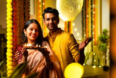 Geleneksel etnik kıyafetli Hintli çift, bayram gecesi Hindu festivali kutlamalarında renkli kadife çiçeklerinin önünde sevinçle dikiliyorlar.