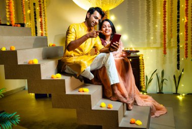 Merdivenlerdeki video görüşmelerine katılan Hintli çift Diwali gecesi kutlamalarında arkadaşlarıyla bağ kuruyor. Dekoratif merdivenlerde Divalar ve çelenklerle oturuyorlar.