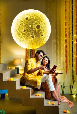 Merdivenlerdeki video görüşmelerine katılan Hintli çift Diwali gecesi kutlamalarında arkadaşlarıyla bağ kuruyor. Dekoratif merdivenlerde Divalar ve çelenklerle oturuyorlar.