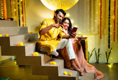 Merdivenlerdeki video görüşmelerine katılan Hintli çift Diwali gecesi kutlamalarında arkadaşlarıyla bağ kuruyor. Dekoratif merdivenlerde Divalar ve çelenklerle oturuyorlar.