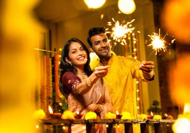 Geleneksel Şenlik Giysileri içinde korkulukların yanında dikilen, Sparkles ve Havai fişeklerle Diwali Gecesinde Neşeli Gülümseyen ve Kutlayan Hintli Çiftler