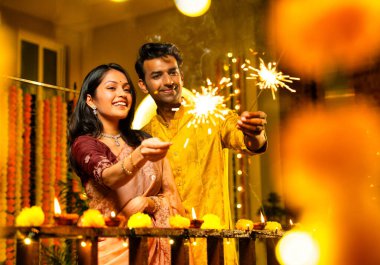 Geleneksel Şenlik Giysileri içinde korkulukların yanında dikilen, Sparkles ve Havai fişeklerle Diwali Gecesinde Neşeli Gülümseyen ve Kutlayan Hintli Çiftler