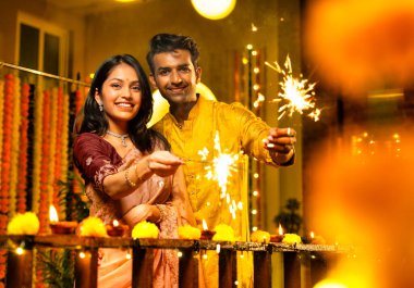 Geleneksel Şenlik Giysileri içinde korkulukların yanında dikilen, Sparkles ve Havai fişeklerle Diwali Gecesinde Neşeli Gülümseyen ve Kutlayan Hintli Çiftler