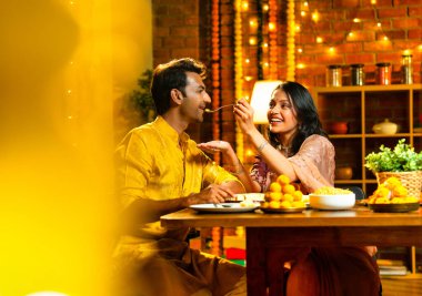 Evde Diwali kutlamaları sırasında tatlı ve abur cubur yiyen çift, geleneksel Hintli karı-koca Hint festivali gecesinde yemek masasında keyifle yemek yiyor.