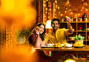 Evde Diwali kutlamaları sırasında tatlı ve abur cubur yiyen çift, geleneksel Hintli karı-koca Hint festivali gecesinde yemek masasında keyifle yemek yiyor.