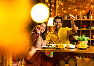 Evde Diwali kutlamaları sırasında tatlı ve abur cubur yiyen çift, geleneksel Hintli karı-koca Hint festivali gecesinde yemek masasında keyifle yemek yiyor.