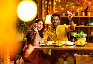 Evde Diwali kutlamaları sırasında tatlı ve abur cubur yiyen çift, geleneksel Hintli karı-koca Hint festivali gecesinde yemek masasında keyifle yemek yiyor.